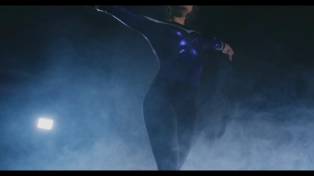 A professional gymnast mid-routine on the balance beam under arena lights and fog